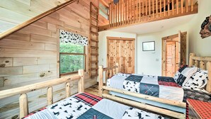Eine Hütte mit zwei Holzbetten, einem Schlafzimmer im Zwischengeschoss und einem Fenster mit Blick auf Grünfläche.