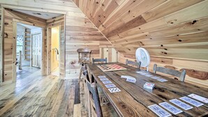 Ein Holzinnenraum mit einem langen Esstisch, der für ein Spiel gedeckt ist, Holzwänden und einem Ventilator auf dem Tisch.