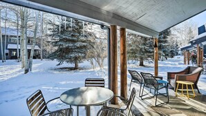A covered outdoor seating area with metal chairs and a table, overlooking a snowy landscape with trees and buildings. - Cozy Vail Valley Townhome - Walk to Riverwalk! (Edwards)