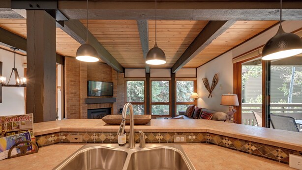 Een moderne keuken met een groot eiland, dubbele spoelbakken en hangende lampen.