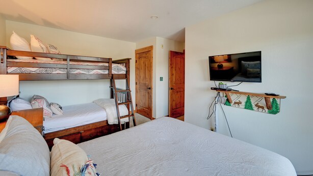 Une chambre avec un lit superposé, un lit simple, un téléviseur fixé au mur et une étagère en bois décorée sur le thème de la nature.