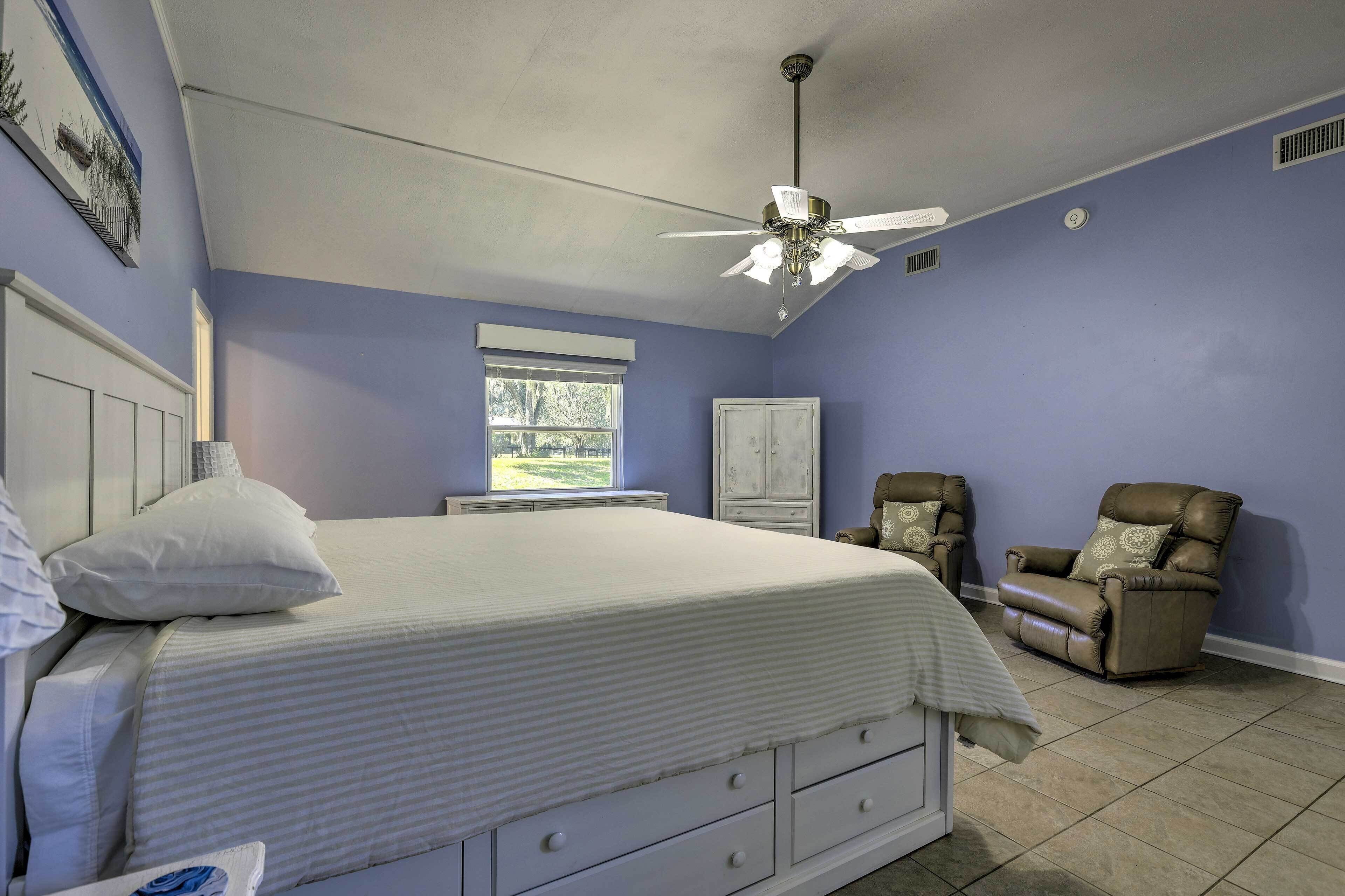 A bedroom with a bed, a ceiling fan, a window, a chair, and a cabinet.