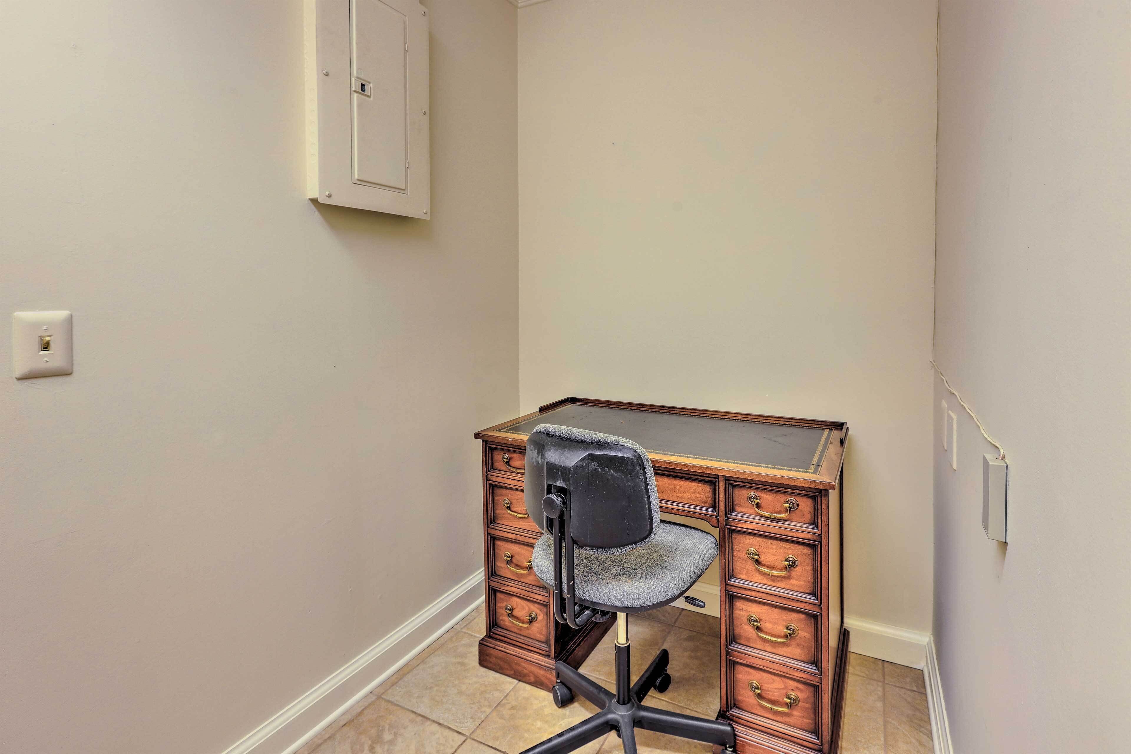 Ein Büro im Eckbereich mit Schreibtisch aus Holz, schwarzem Bürostuhl und einer weißen Steckdose an der Wand.