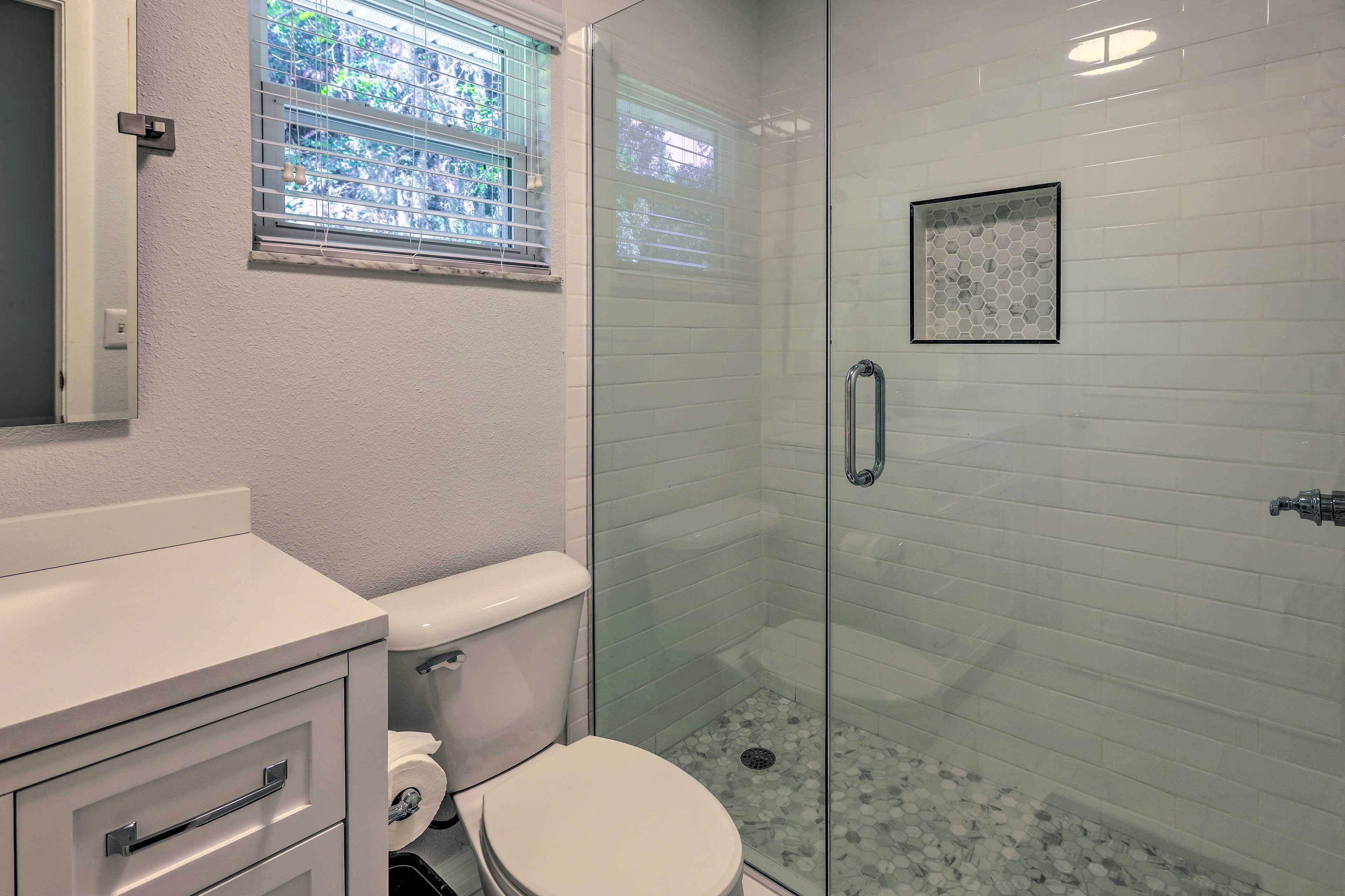 A bathroom with a toilet, a glass-enclosed shower, and a window with blinds.