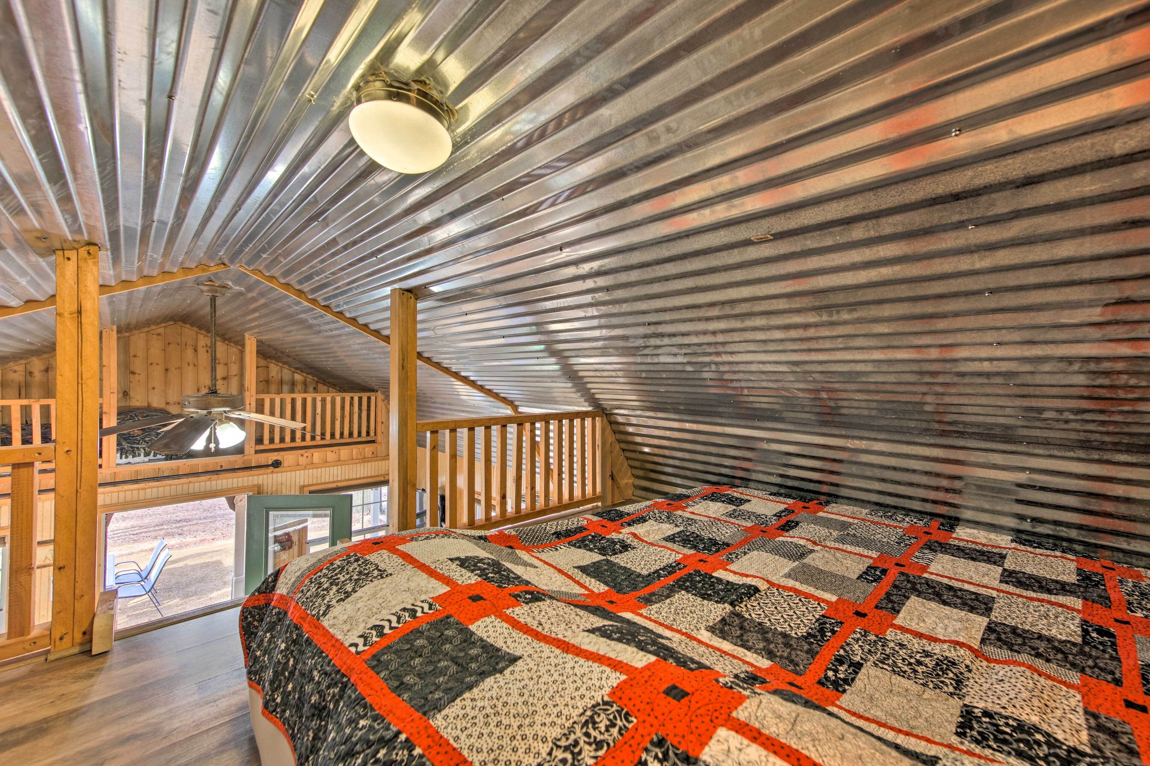 A cozy attic bedroom with a wooden ceiling, a large quilt, and a balcony with a view.
