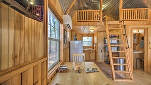 A wooden cabin interior with a dining area, kitchen, and a loft bedroom with a wooden staircase. - Lakefront Cabin w/ 2 Lofts, Boats on 4 Acres (Winnsboro)
