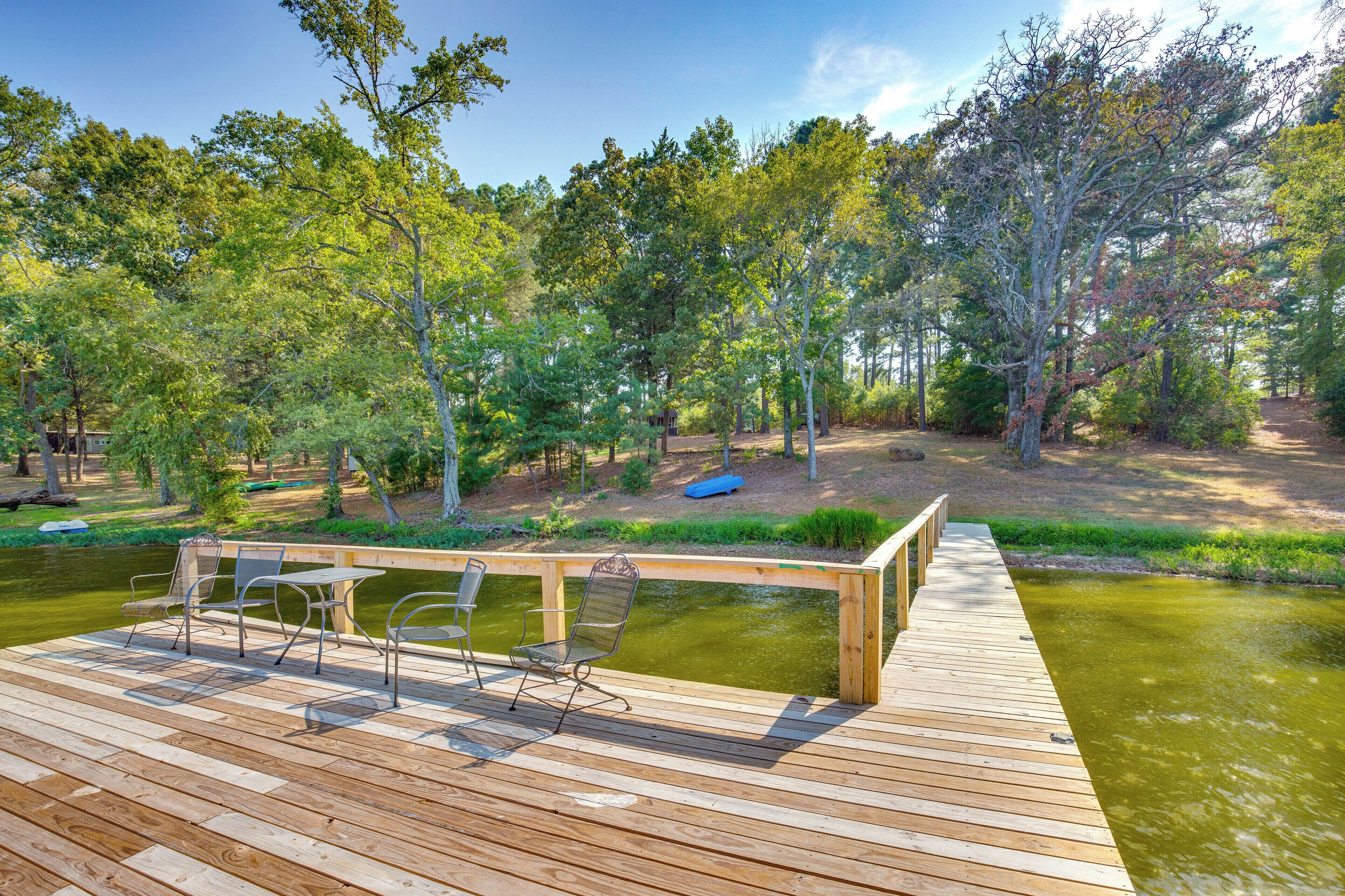 A wooden deck with metal chairs and a table overlooking a pond, surrounded by trees.
