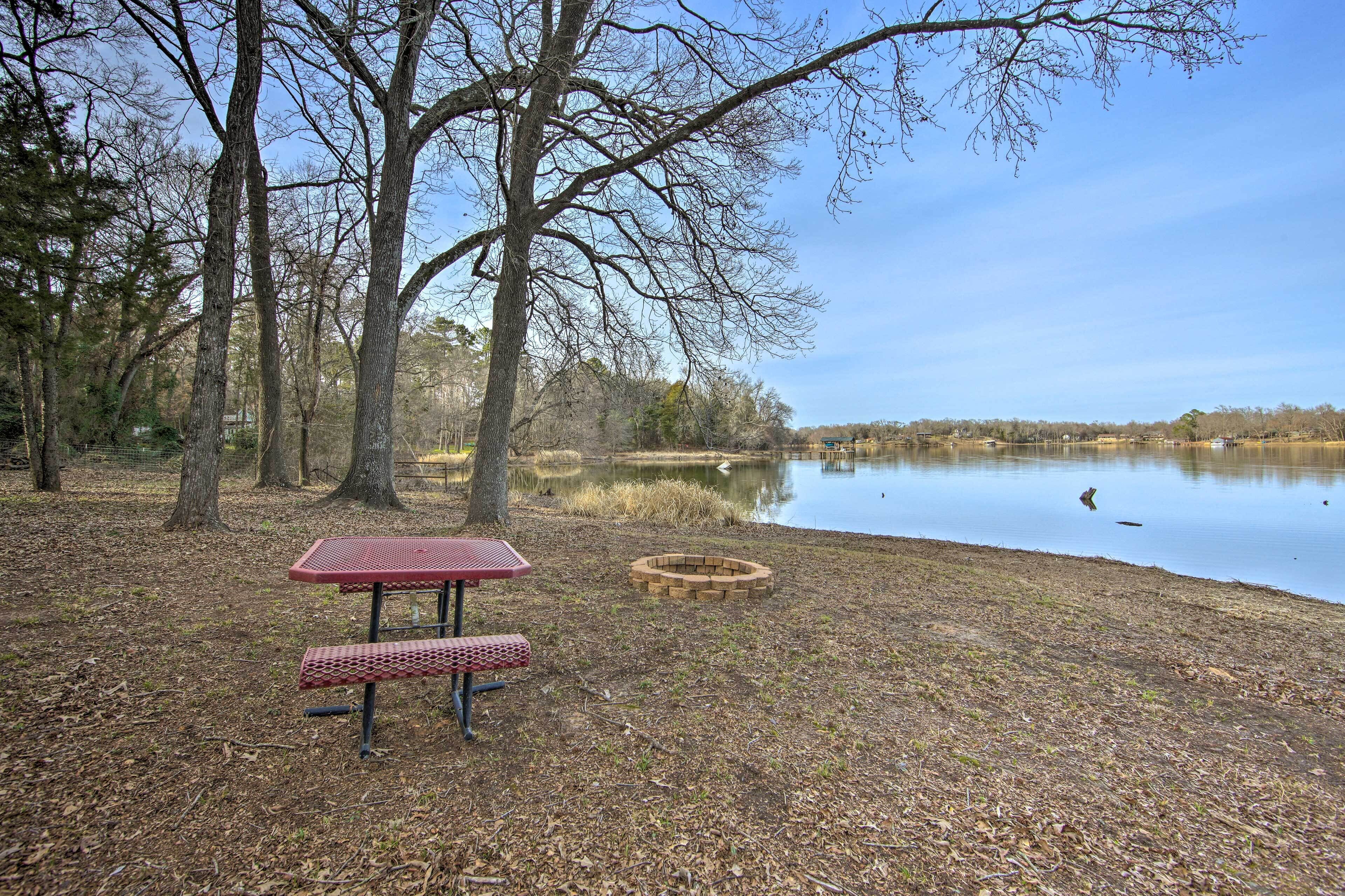 A picnic table and benches in a park with a lake and trees.