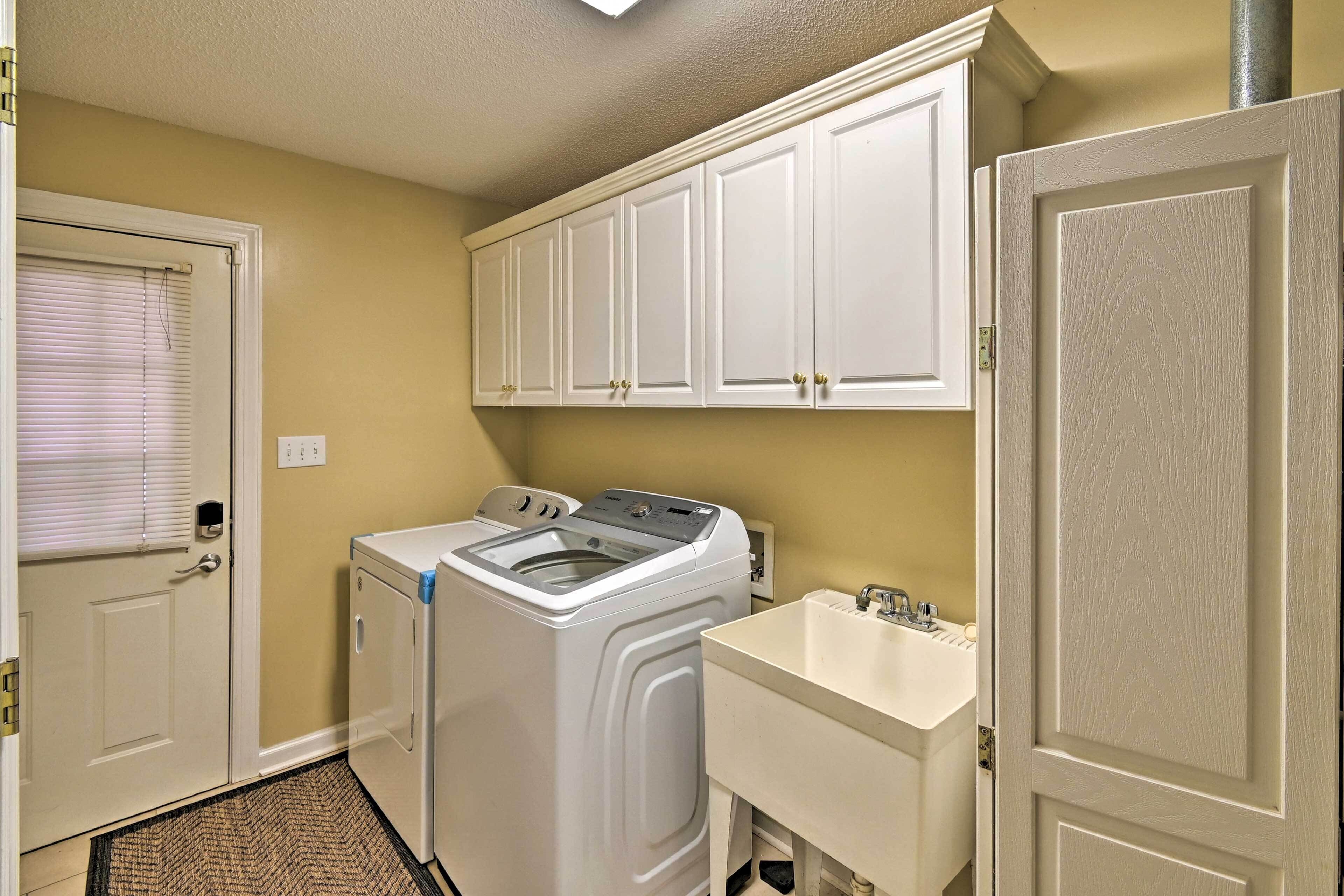 A laundry room with a washing machine, a sink, and white cabinets.
