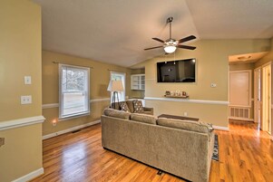 A living room with a sofa, a ceiling fan, a flat-screen TV, and wooden flooring.