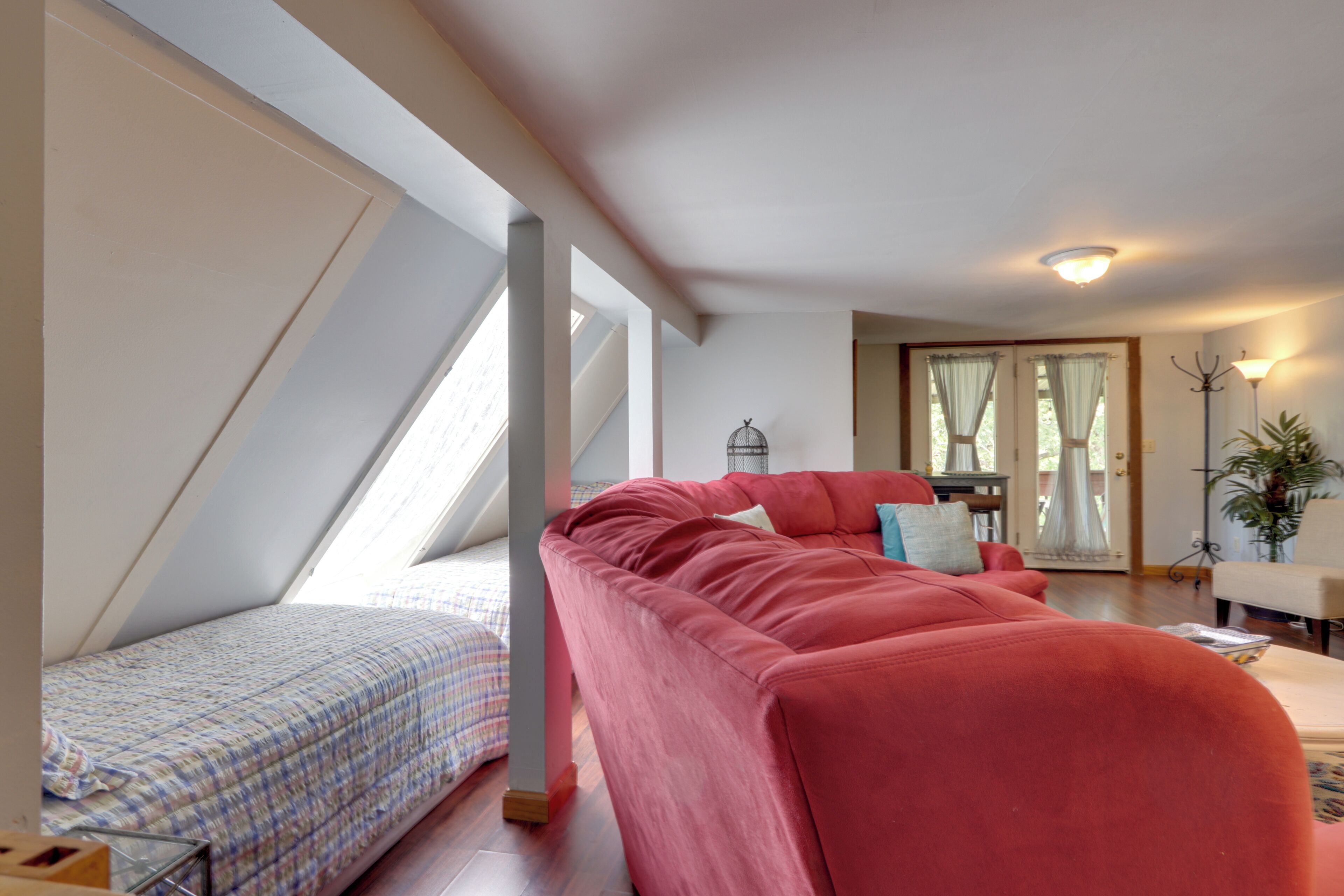 A room with a red sofa, a small bed with a checkered bedspread, and a window with curtains.