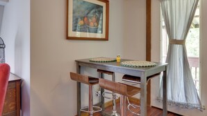 Un comedor con una mesa y dos taburetes altos, un cuadro en la pared y una ventana con cortinas.