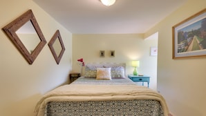 Un dormitorio con cama, dos espejos en la pared, una mesita de noche con lámpara y cuadros enmarcados.