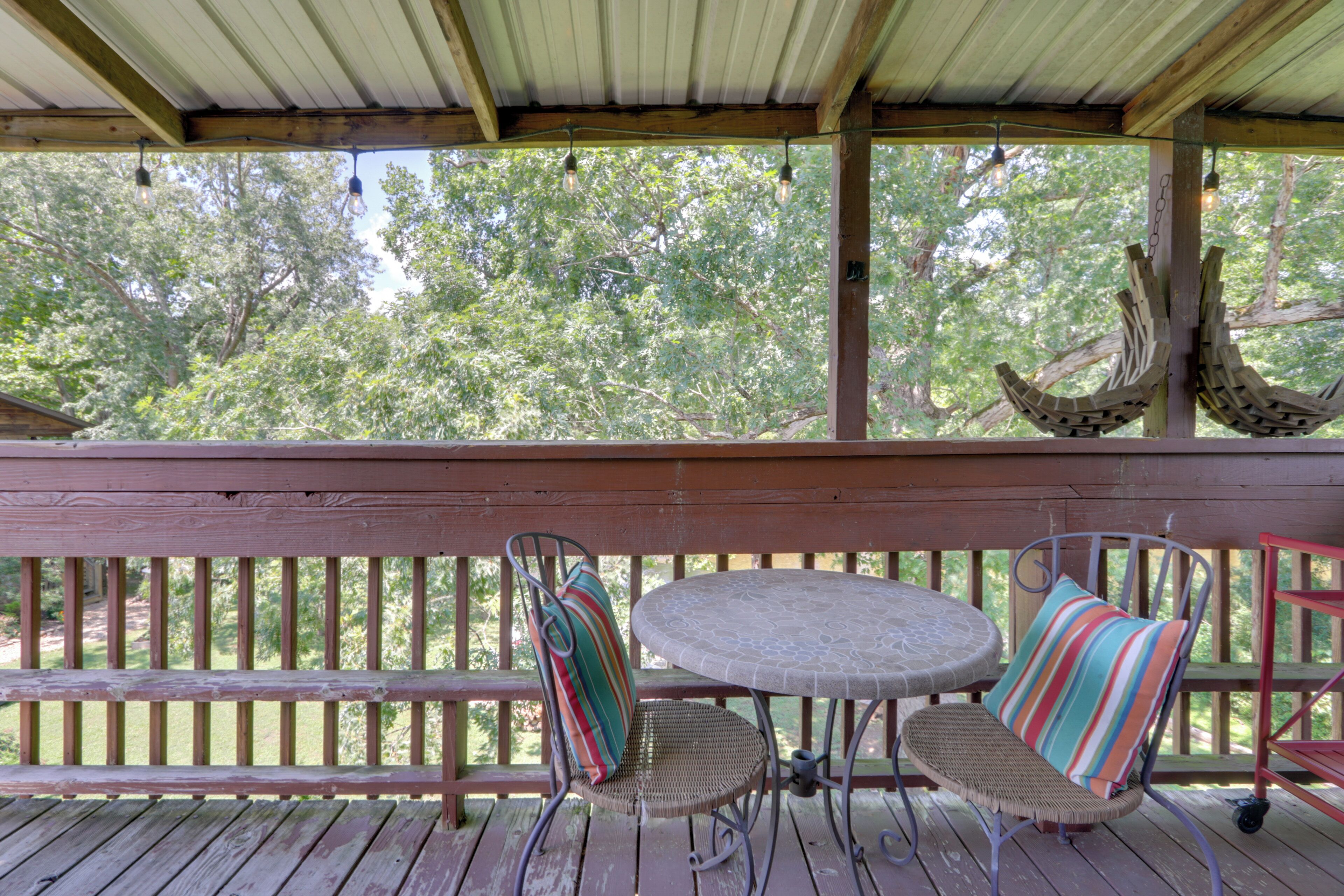 A wooden deck with a round table and two wicker chairs with striped cushions.