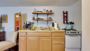 Una cocina funcional con gabinetes de madera, una estufa blanca y repisas sobre el lavabo con platos y frascos.