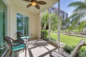 A balcony with wicker chairs, a ceiling fan, and a view of a green lawn and buildings. - Waterfront Punta Gorda Condo w/ Pool Access! (Punta Gorda)