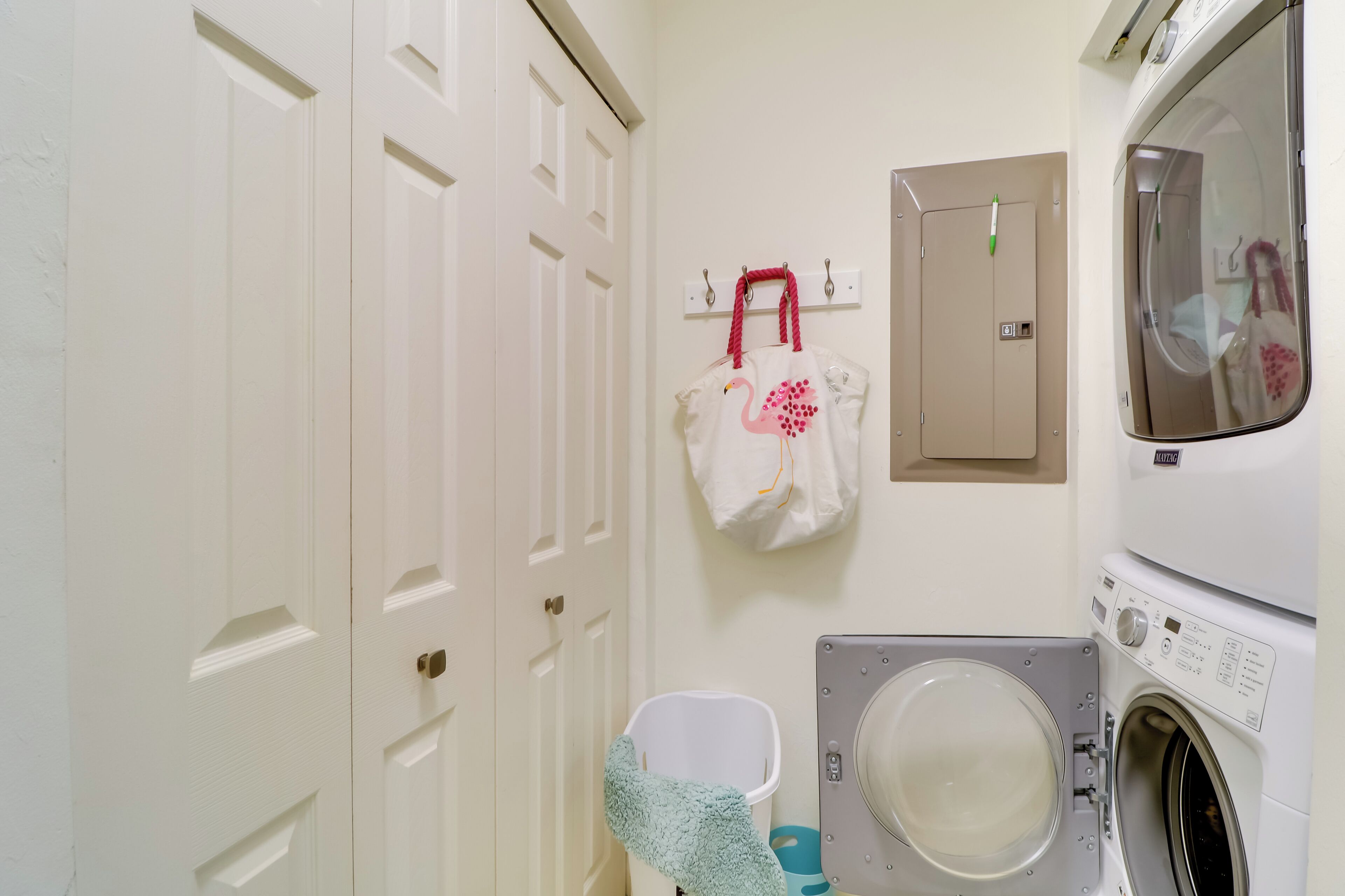 A laundry room with a washing machine, a drying machine, a white door, and a wall-mounted drying rack with a white bag.