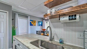 A kitchen with a granite countertop, stainless steel sink, and wooden shelves above the counter.