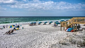 A beach with umbrellas, lounge chairs, and a wooden pier.