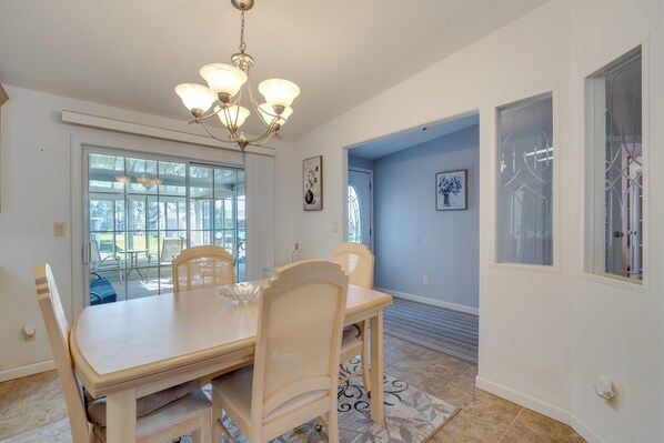A dining area with a wooden table and chairs, a chandelier, and large windows. - Near Golf & Dining: Wildwood Vacation Rental! (Wildwood)