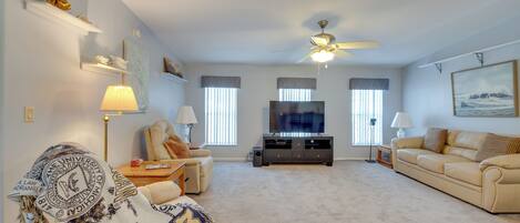 A living room with a beige sofa, a coffee table, a television, and a ceiling fan.