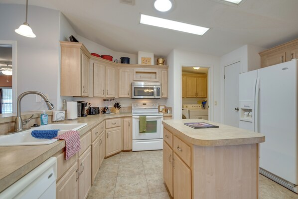 A kitchen with wooden cabinets, a white refrigerator, a microwave, and a sink. - Near Golf & Dining: Wildwood Vacation Rental! (Wildwood)