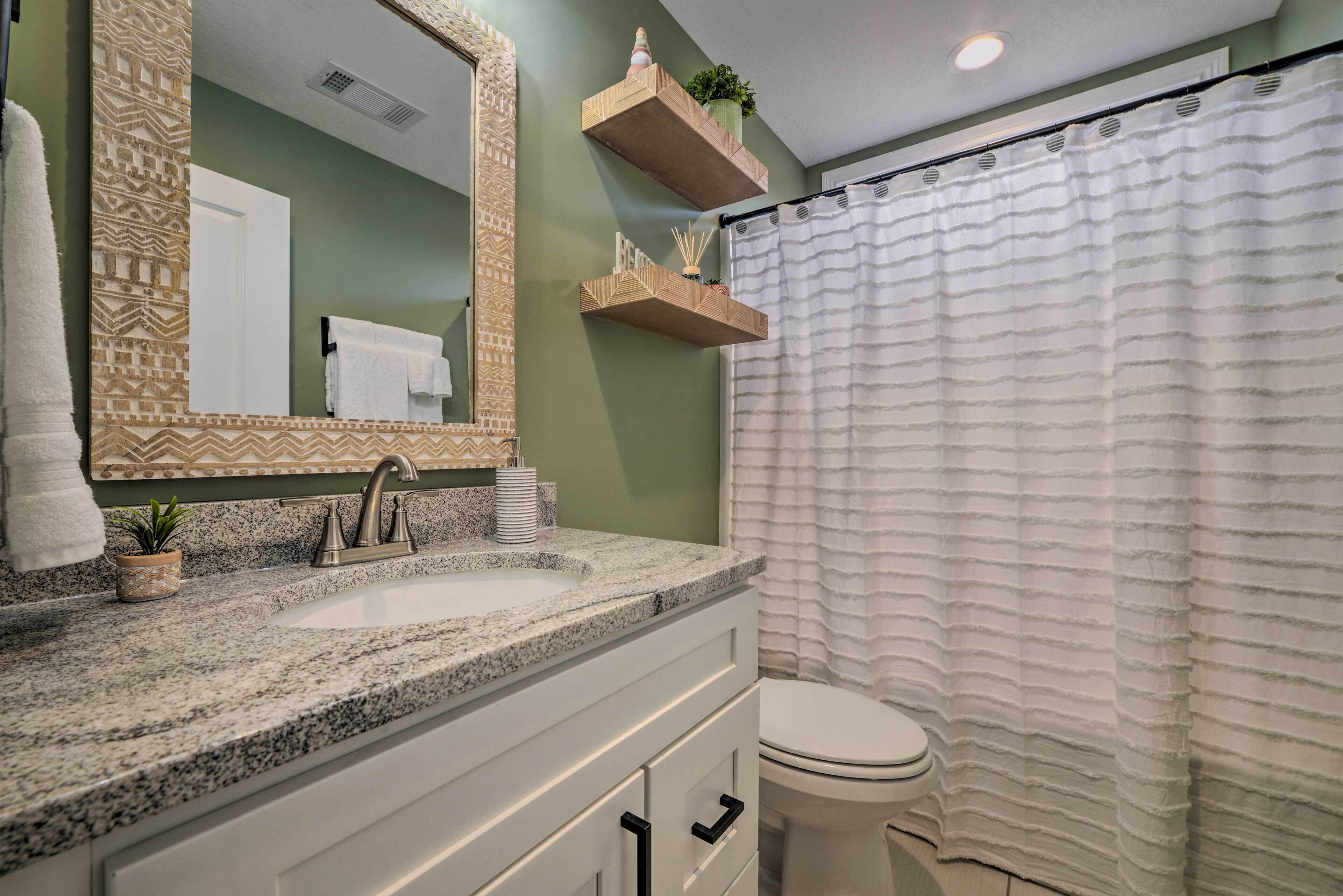 A bathroom with a granite countertop sink, a mirror with a patterned frame, a toilet, and a shower curtain.
