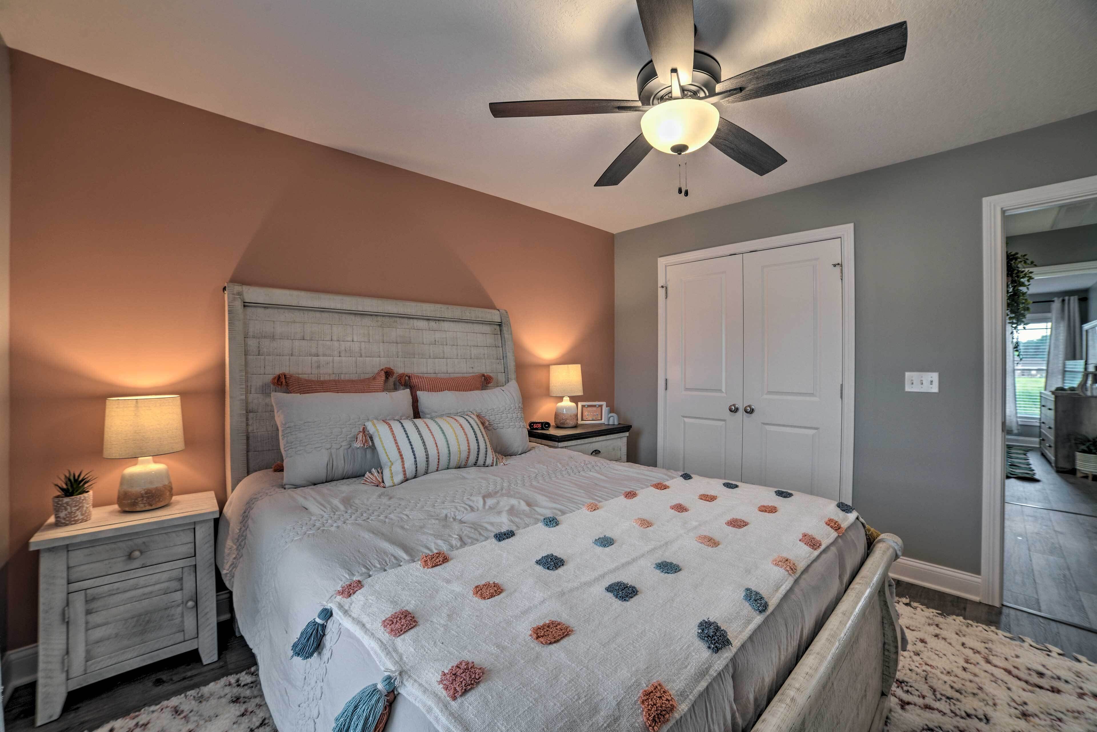 A bedroom with a bed, nightstands, a ceiling fan, and a door.