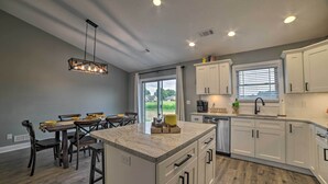 A modern kitchen with white cabinets, a granite countertop island, and a dining area with wooden chairs. - Cozy Murray Retreat Near MSU & Local Eateries (Murray)