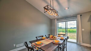 A dining room with a wooden table set for four, surrounded by chairs, a modern chandelier, and a view through large windows. - Cozy Murray Retreat Near MSU & Local Eateries (Murray)
