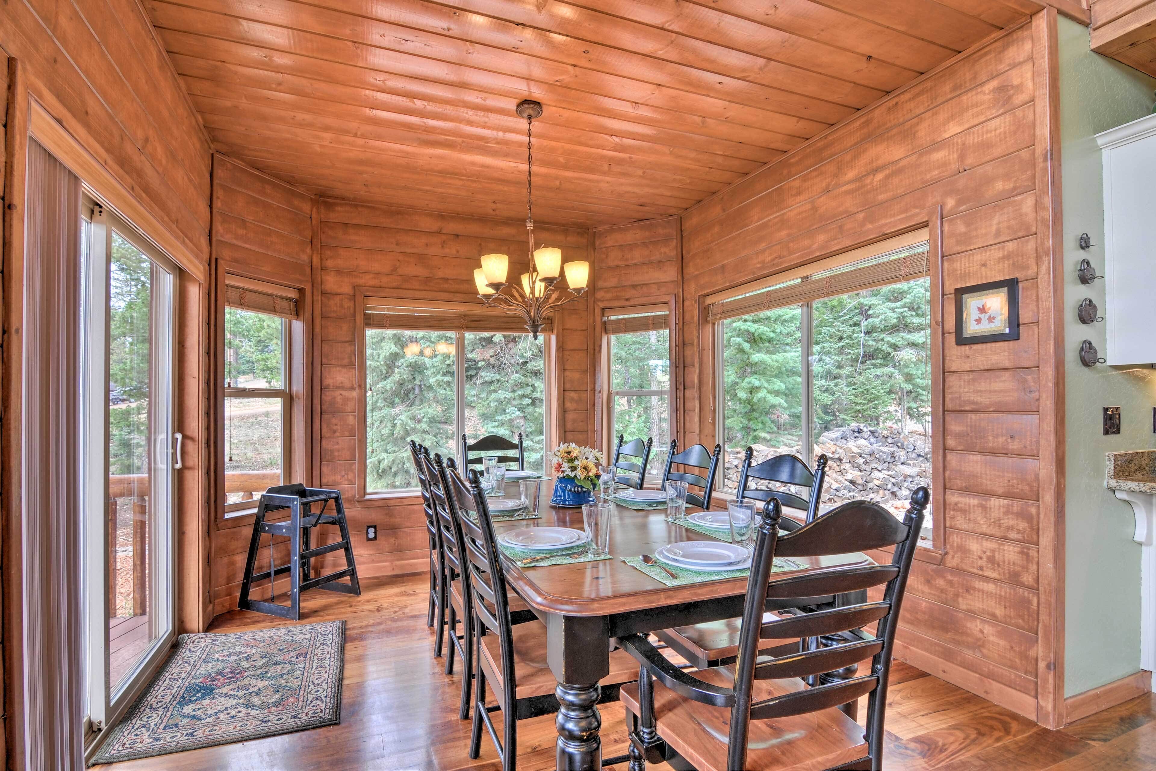 Une salle à manger en bois avec une table dressée pour six personnes, de grandes fenêtres et un lustre.