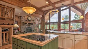Una cocina rústica con una isla central, vigas de madera, pared de piedra y ventanas amplias.