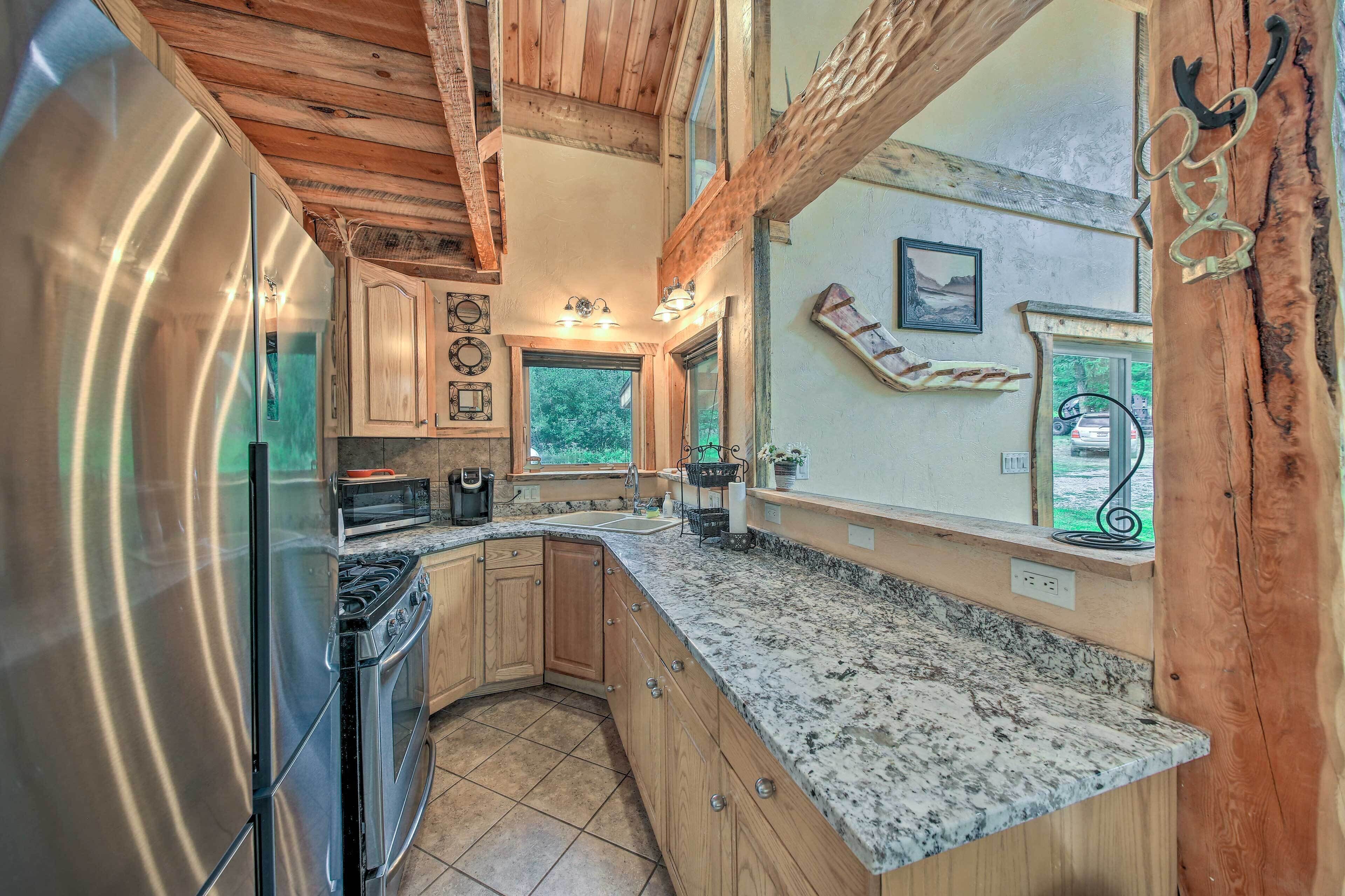 A kitchen with wooden cabinets, a stainless steel refrigerator, granite countertops, and a view of the outdoors.