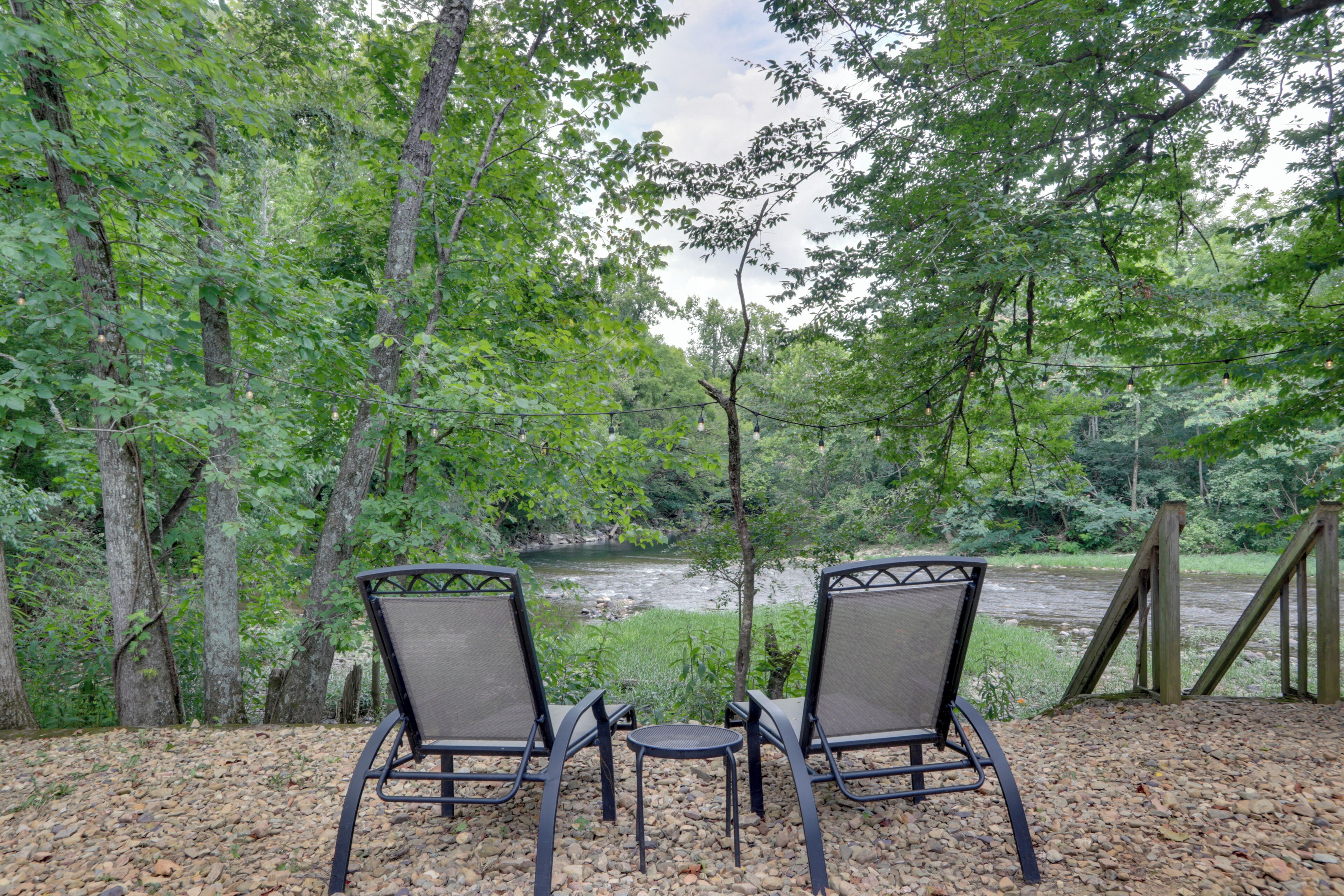 Two chairs facing a river with a wooden deck and gravel path.