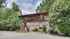 A rustic log cabin with a wooden porch, surrounded by lush greenery and flowering bushes. - Riverfront Couple's Retreat in Smoky Mountains! (Townsend)