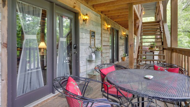 A covered outdoor area with a wooden deck, metal chairs with red cushions, and a glass table. - Riverfront Couple's Retreat in Smoky Mountains! (Townsend)
