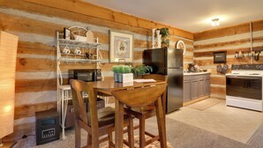 A log cabin-style kitchen with wooden walls, a dining table with chairs, a refrigerator, a stove, and a coffee maker. - Riverfront Couple's Retreat in Smoky Mountains! (Townsend)