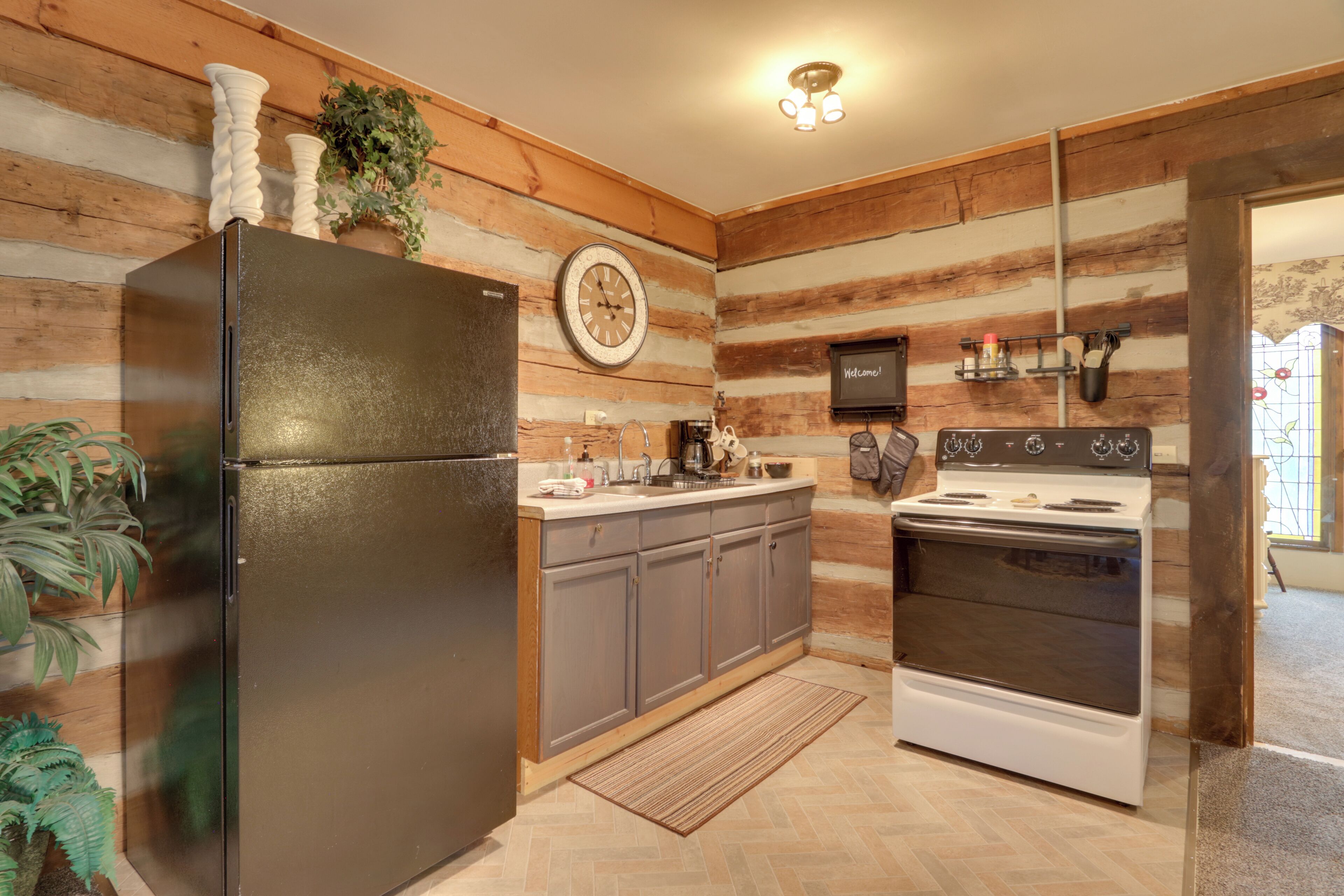 A kitchen with wooden walls, a black refrigerator, a stove, and a clock on the wall.