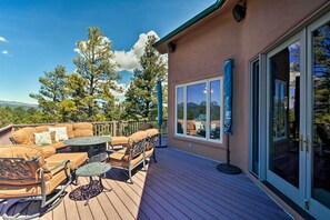 Um terraço com mobiliário de exterior, uma porta de vidro e vista para árvores e montanhas.