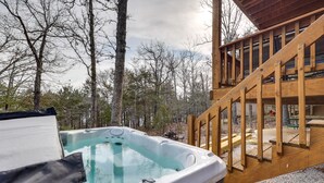Un bain à remous situé dans un espace boisé, avec une terrasse en bois et un escalier menant à un porche abrité.
