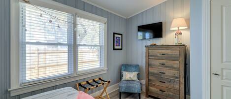A bedroom with a bed, a chair, a dresser, a TV, and a window with blinds.