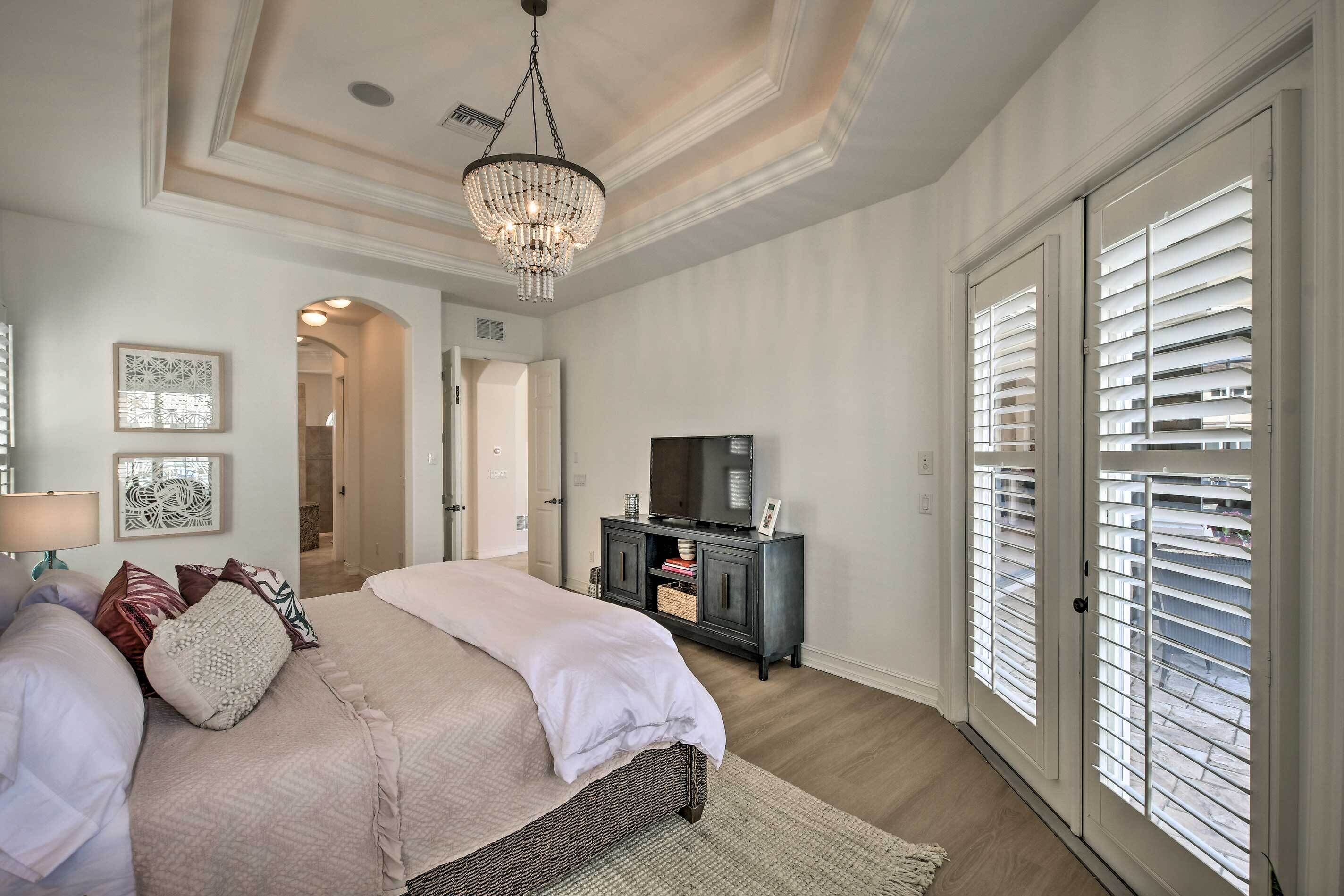 A bedroom with a large bed, a chandelier, a television, and a sliding door with blinds.