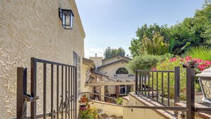 A narrow outdoor corridor with a metal gate, potted plants, and a small patio area with a brick wall and a white railing. - 16 Mi to Beaches & Wineries! Chic Peaceful Retreat (Santa Paula)