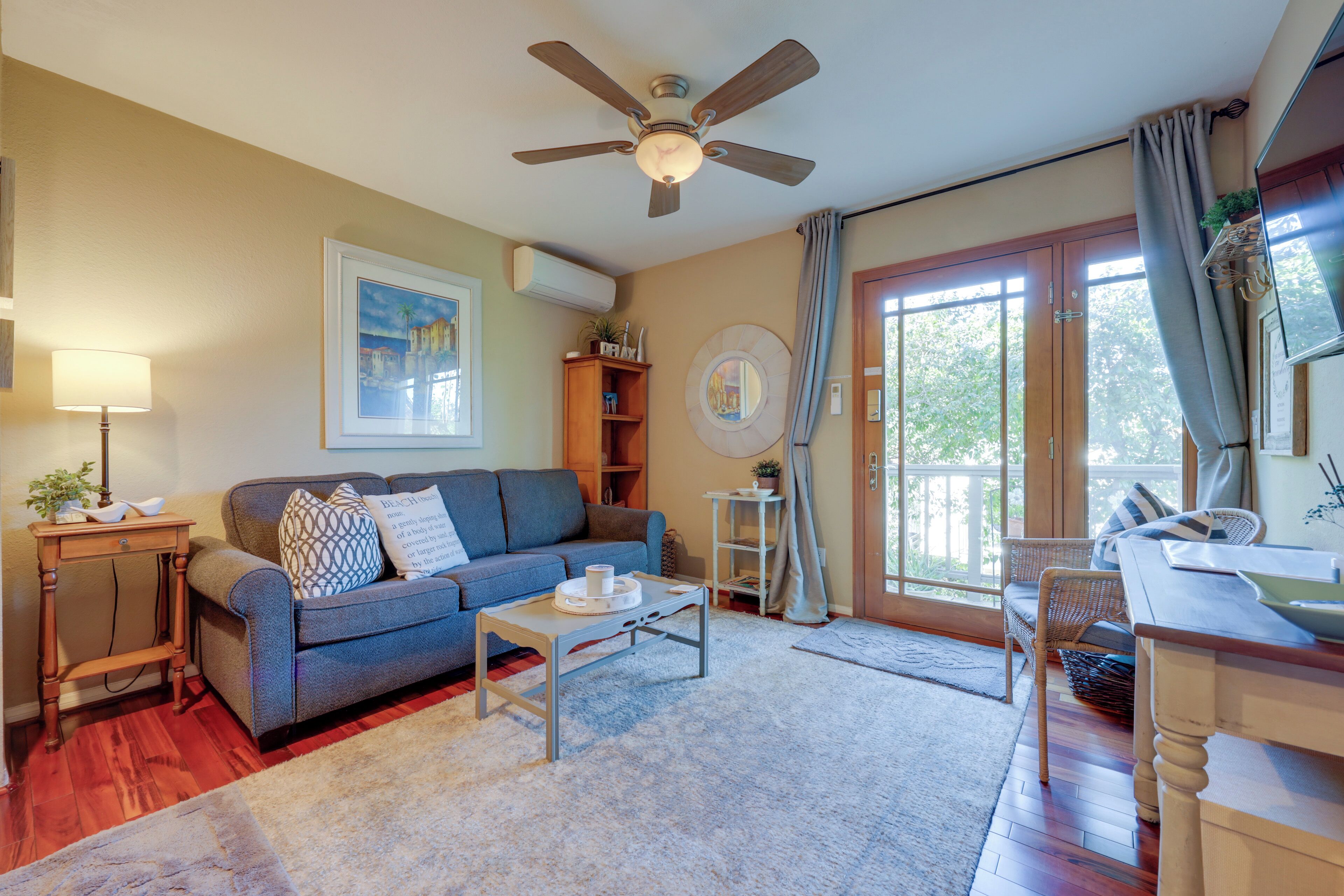 A living room with a sofa, coffee table, and a ceiling fan. There is a window with curtains and a door leading outside.