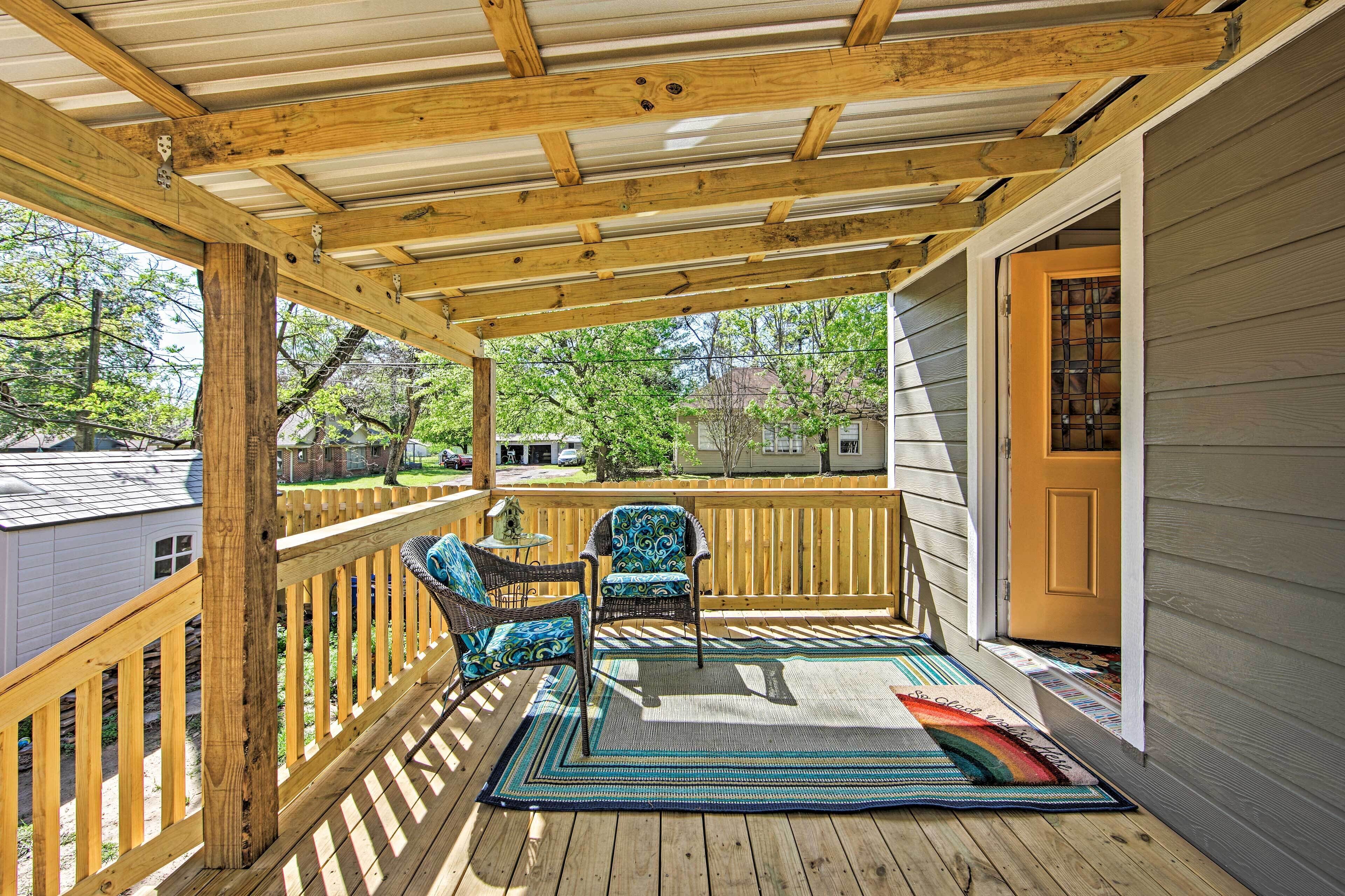 A covered porch with wooden railings, a bench, and a chair.