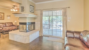 A living room with a fireplace, leather sofas, and a large window with curtains. - Covered Deck & 2-story Dock: Lake Travis Home! (Leander)