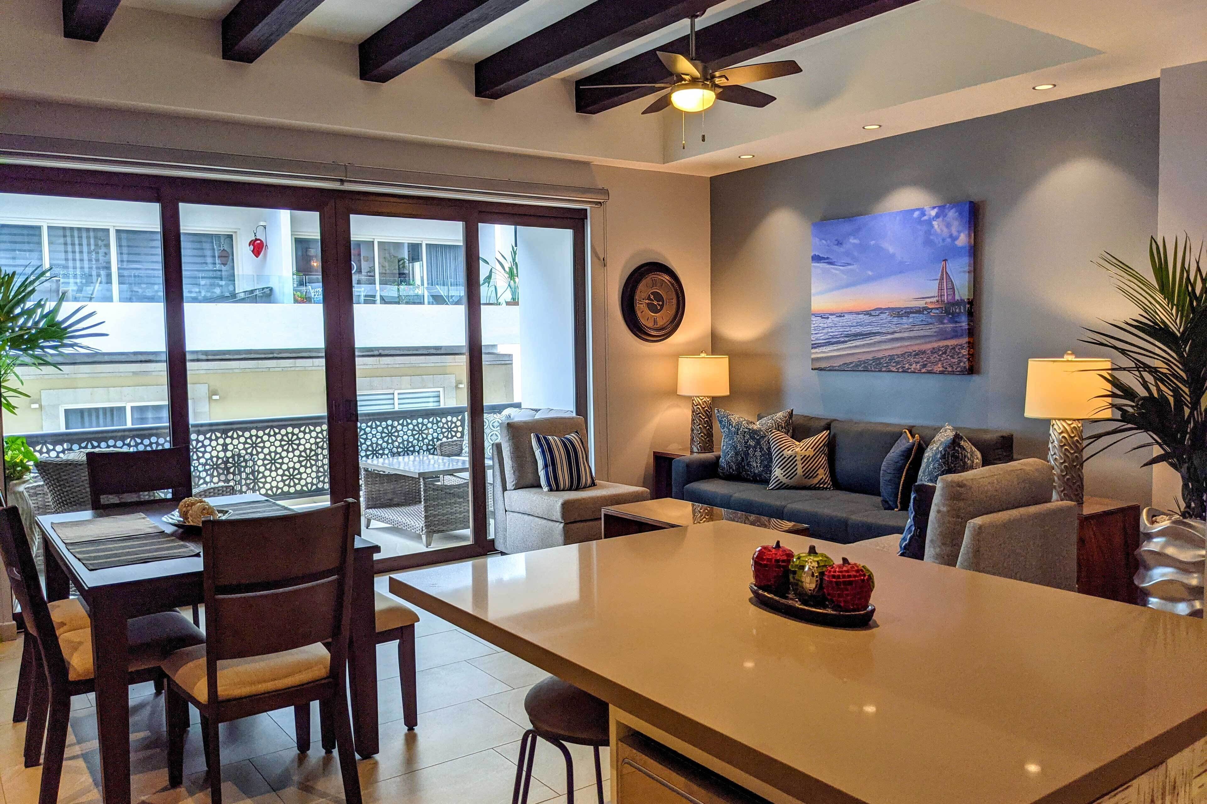 Una sala moderna con sofá, mesa de comedor y sillas. Hay un cuadro en la pared y un ventilador de techo.