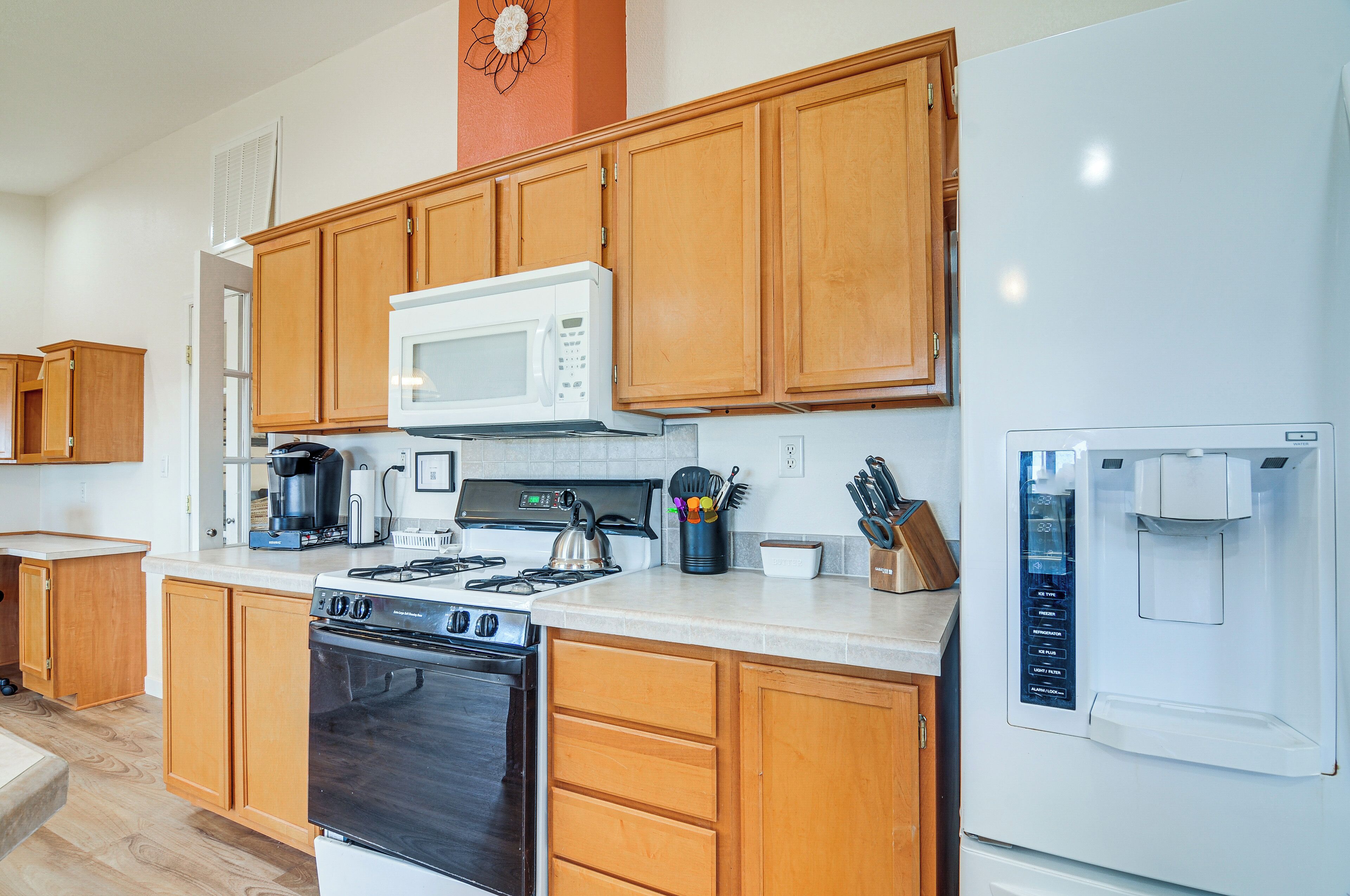 A modern kitchen with wooden cabinets, a microwave, stove, coffee maker, and a refrigerator with a water dispenser.