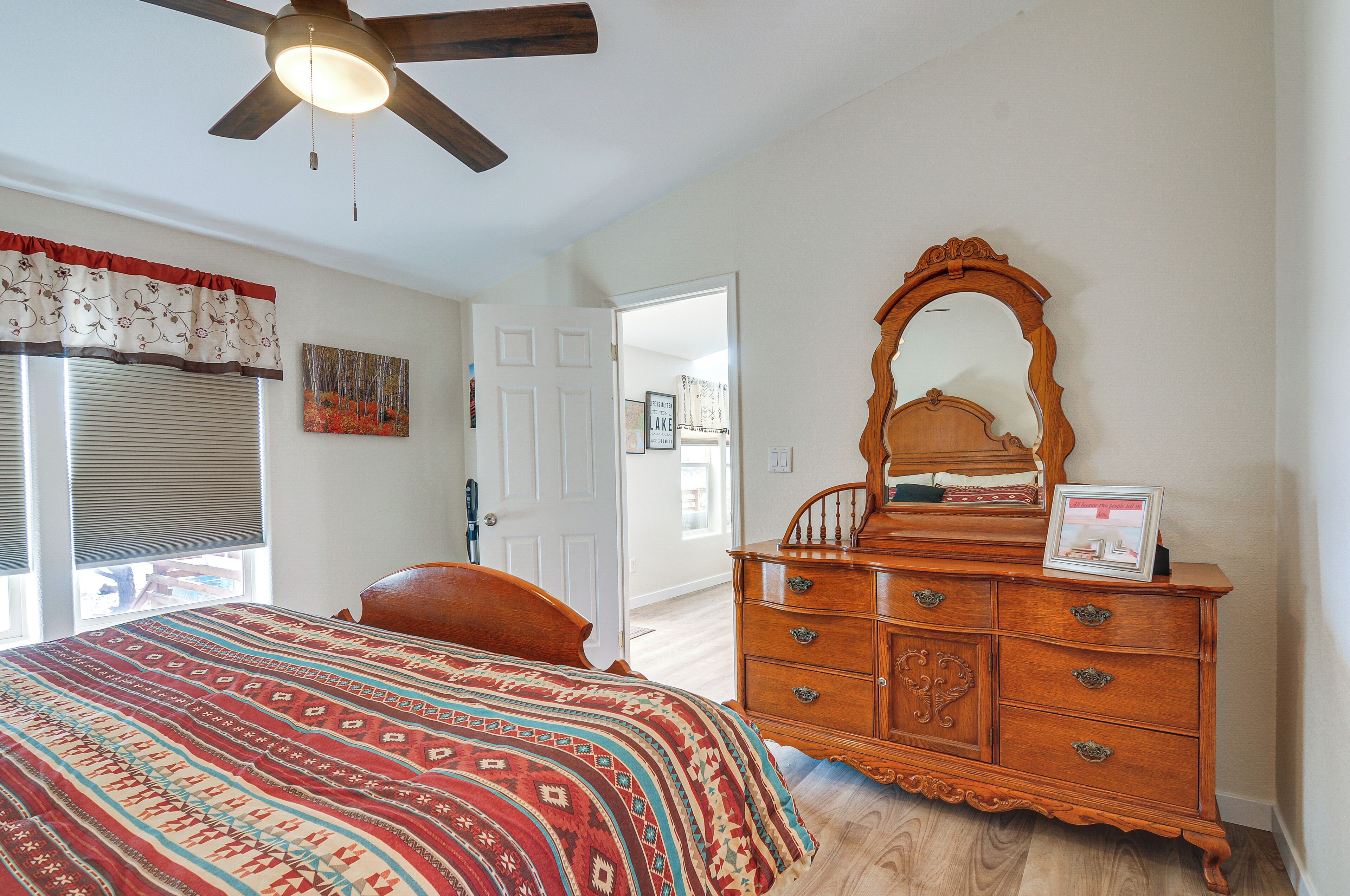 A bedroom with a bed, dresser, mirror, and ceiling fan.