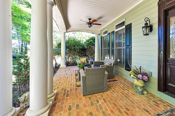 A covered porch with wicker furniture, a ceiling fan, and a brick floor.